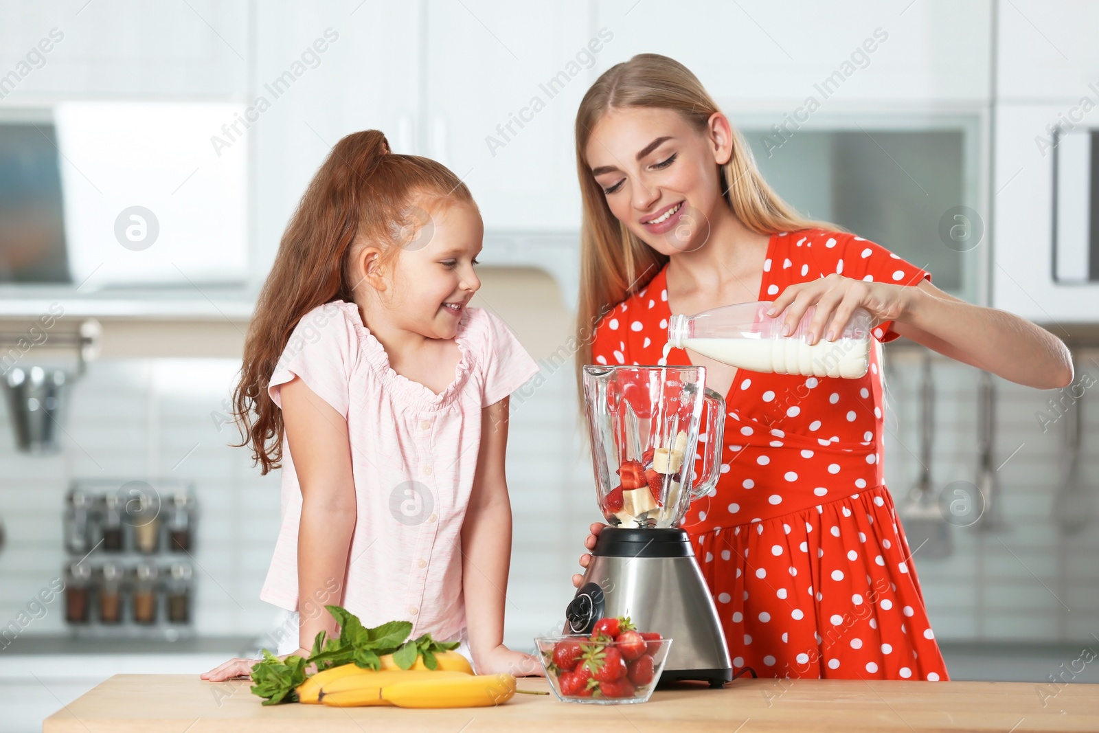 Photo of Mother and daughter preparing delicious milk shake in kitchen