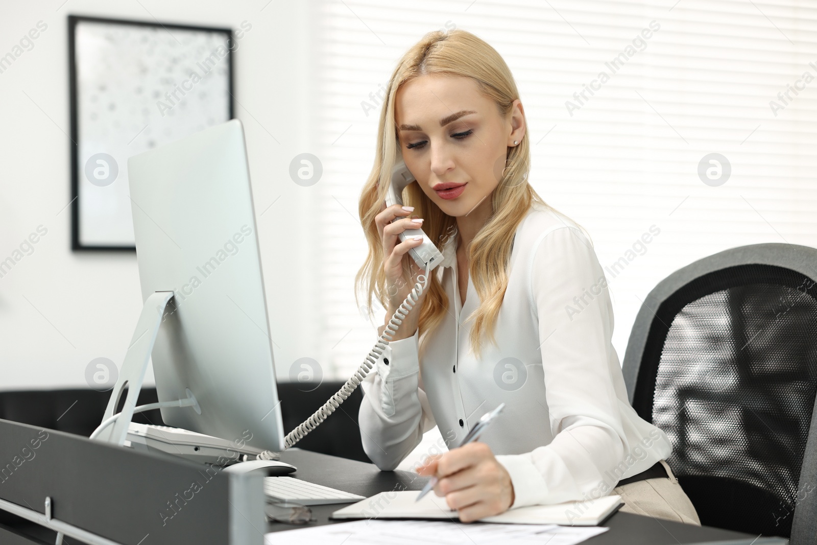 Photo of Secretary talking on phone and taking notes at table in office