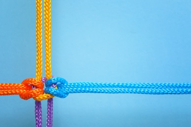 Different ropes tied together with knot on color background. Unity concept