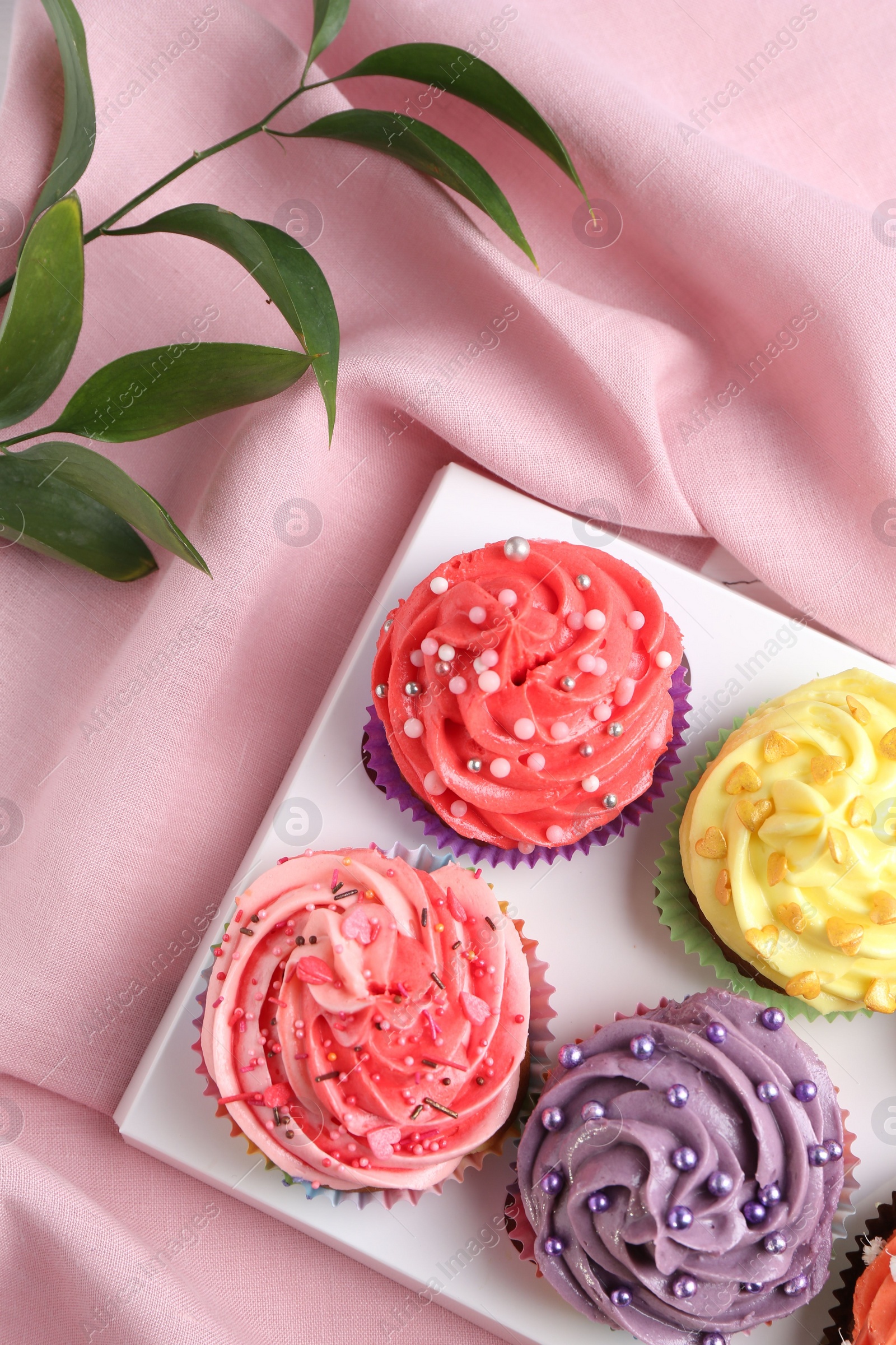 Photo of Delicious cupcake with bright cream on pink fabric, top view