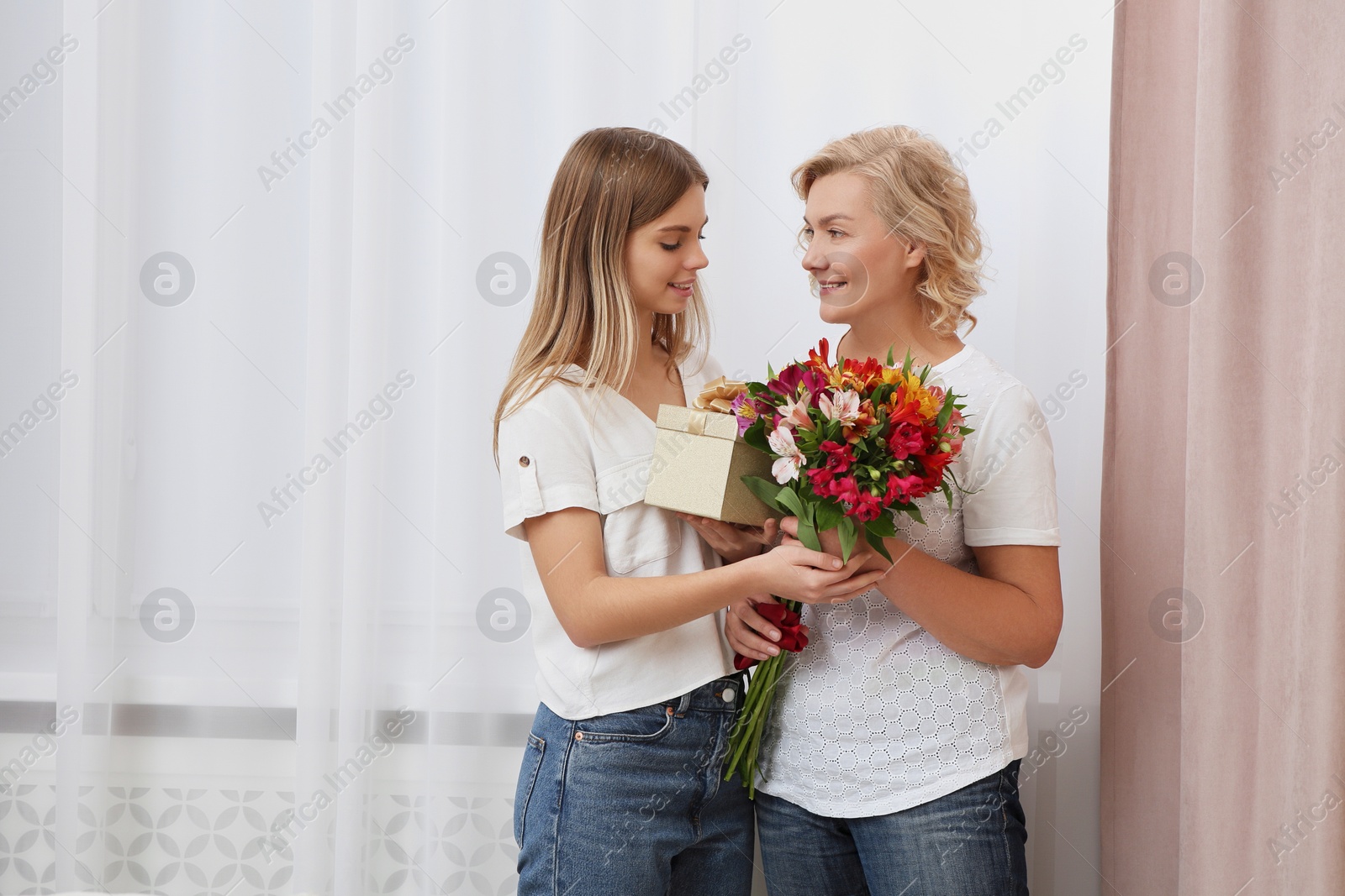 Photo of Young daughter congratulating her mom with flowers and gift at home. Happy Mother's Day