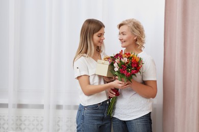 Young daughter congratulating her mom with flowers and gift at home. Happy Mother's Day