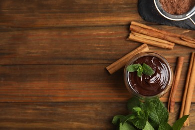 Photo of Glass of delicious hot chocolate with fresh mint and cinnamon sticks on wooden table, flat lay. Space for text