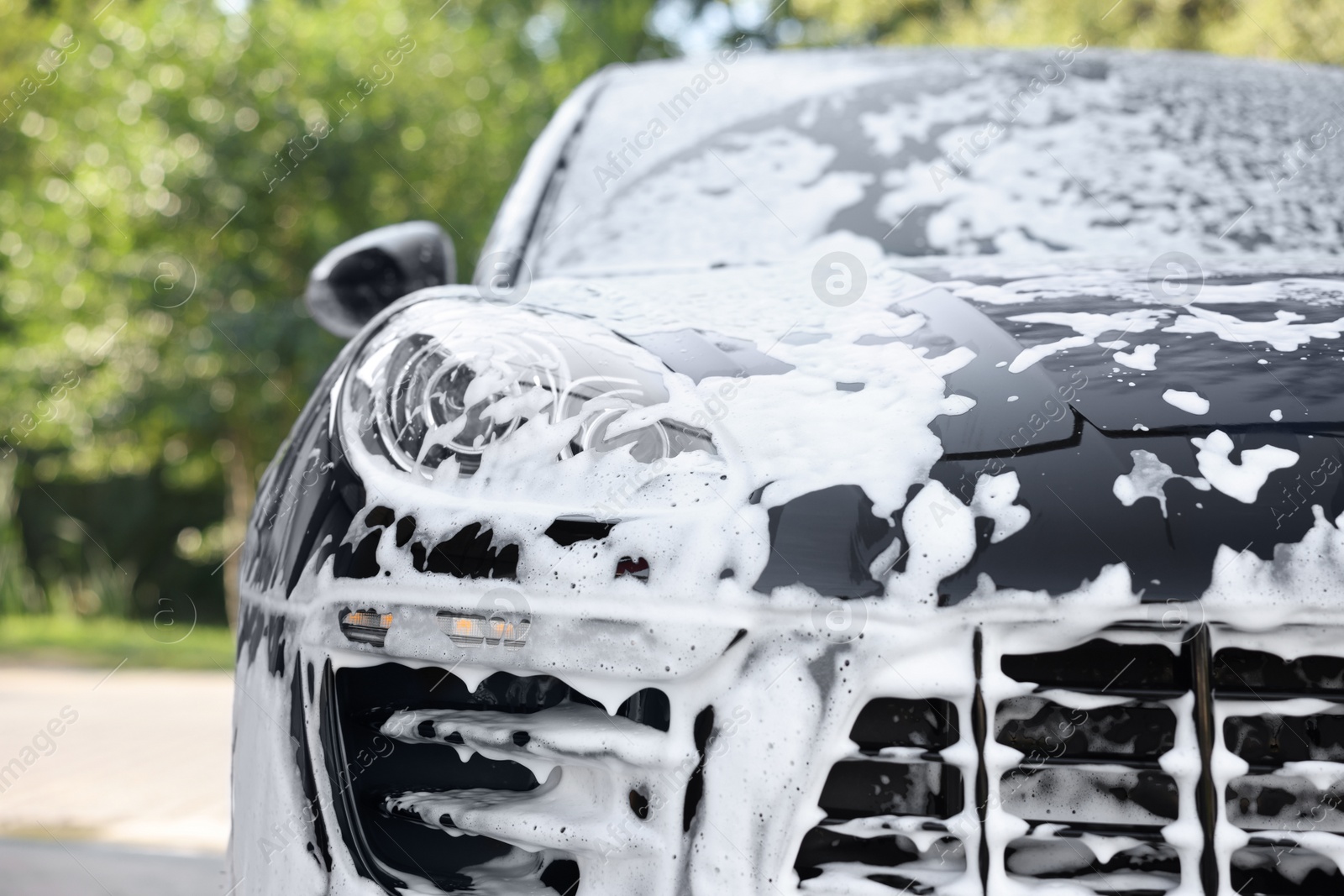 Photo of Auto covered with cleaning foam at outdoor car wash, closeup