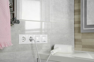 Photo of Hairdryer plugged into power socket on light grey wall in bathroom