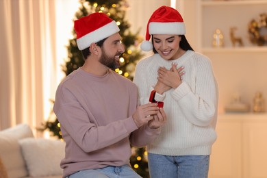 Making proposal. Man with engagement ring surprising his girlfriend at home on Christmas
