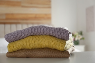 Stack of knitted sweaters on white table indoors, closeup