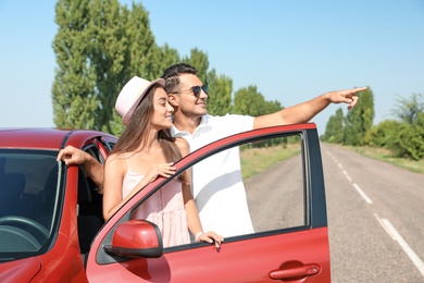 Happy young couple standing near car on road