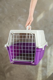 Photo of Woman holding violet pet carrier against grey wall, closeup