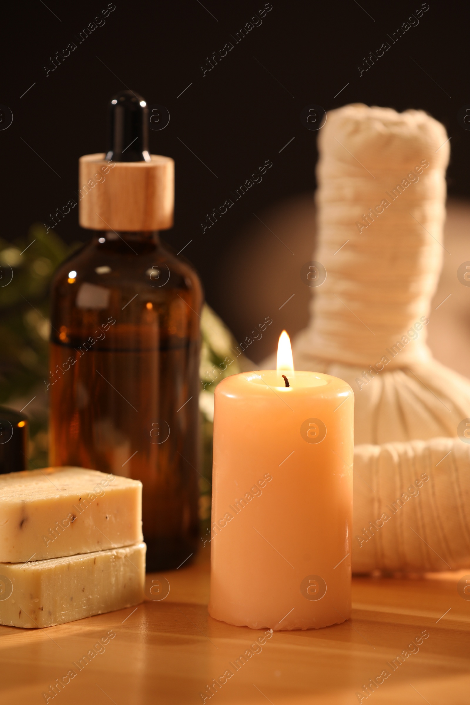 Photo of Spa composition. Cosmetic products, herbal bags and burning candle on wooden table, closeup