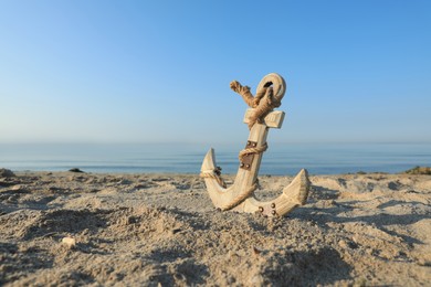 Photo of Wooden anchor with rope on sand near sea. Space for text