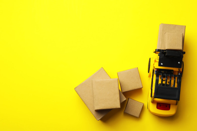 Photo of Top view of toy forklift with boxes on yellow background, space for text. Logistics and wholesale concept