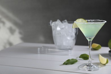 Photo of Delicious Margarita cocktail in glass and lime on white wooden table, space for text