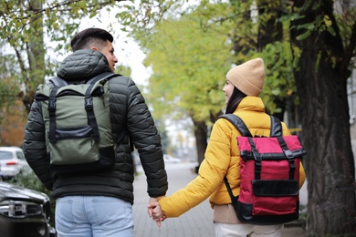 Photo of Couple with travel backpacks on city street, back view. Urban trip