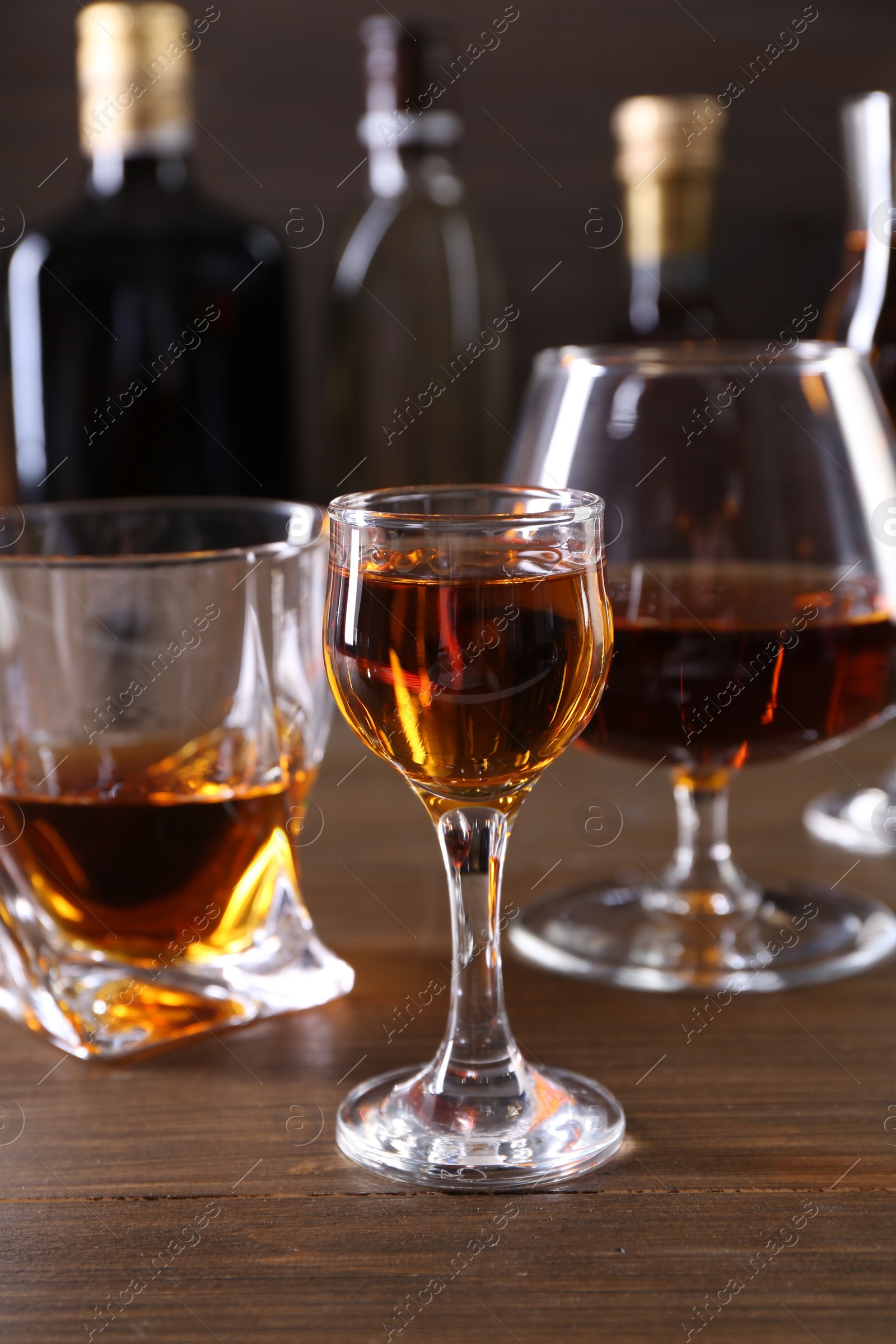 Photo of Different delicious liqueurs in glasses and bottles on wooden table