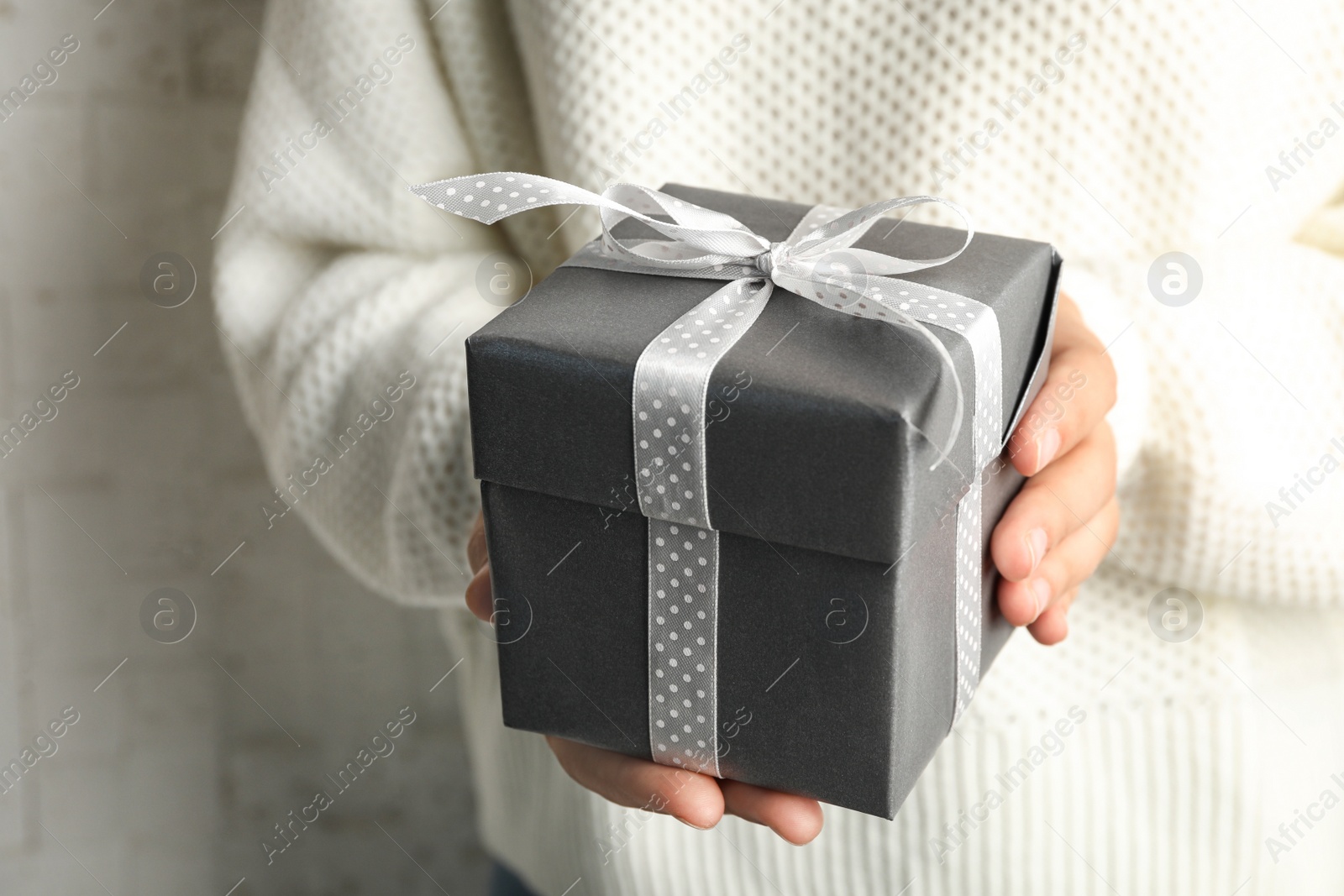 Photo of Young woman holding Christmas gift on light background, closeup