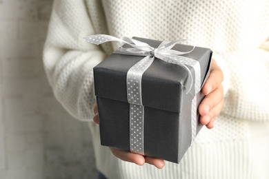 Young woman holding Christmas gift on light background, closeup