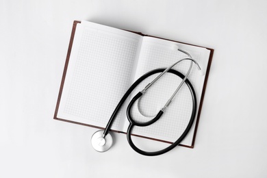 Stethoscope and open notebook with space for text on white background, top view. Medical students stuff