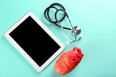 Photo of Stethoscope, tablet and model of heart on color background. Heart attack concept