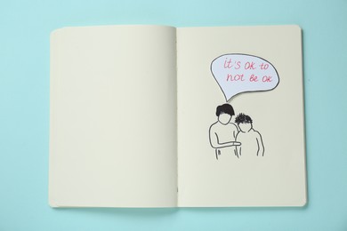 Photo of Card with phrase It`s Ok to Not Be Ok, drawing of mother and her son in notebook on light turquoise background, top view