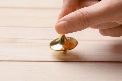 Photo of Woman playing with metal spinning top at light wooden table, closeup