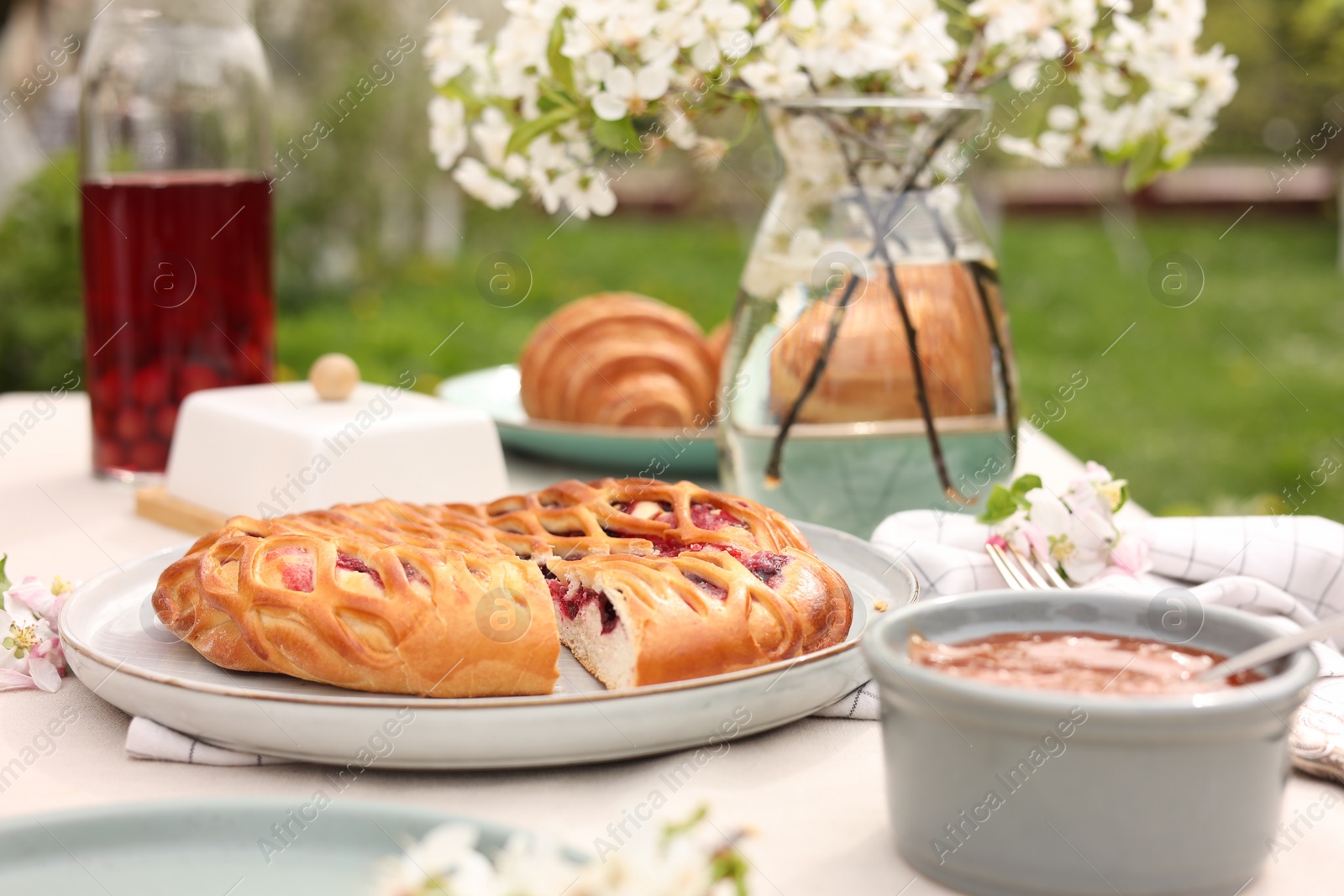 Photo of Stylish table setting with beautiful spring flowers, fruit drink and pie in garden