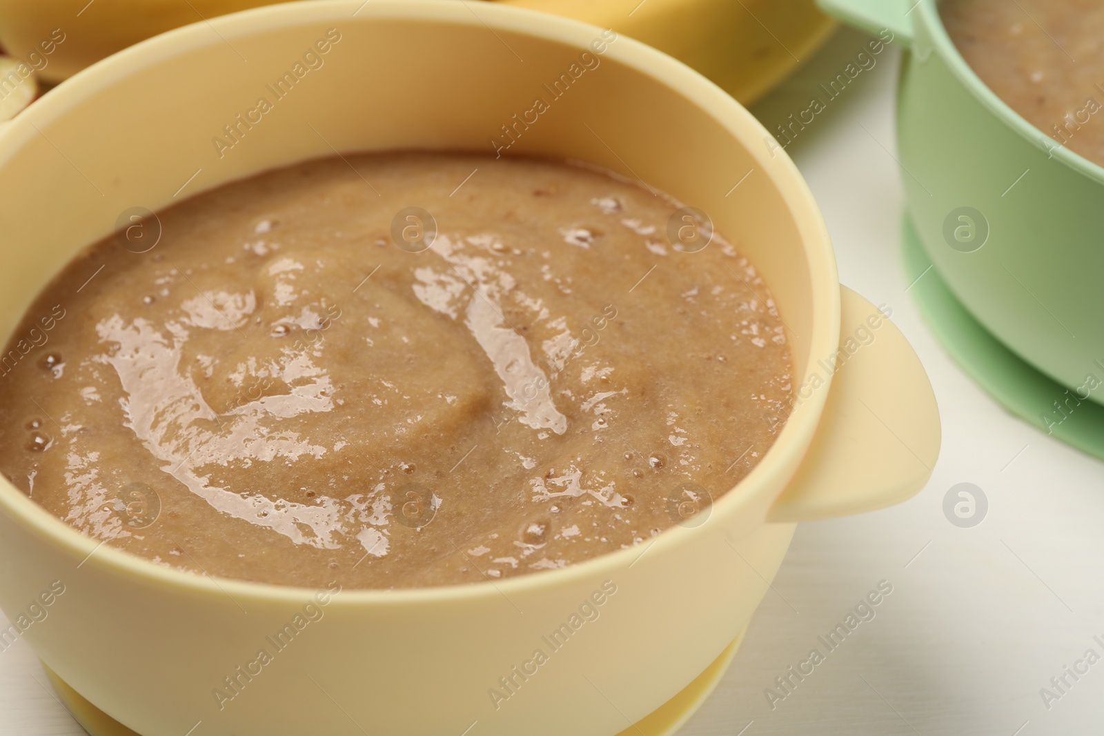 Photo of Baby food. Bowl with banana puree on white table, closeup