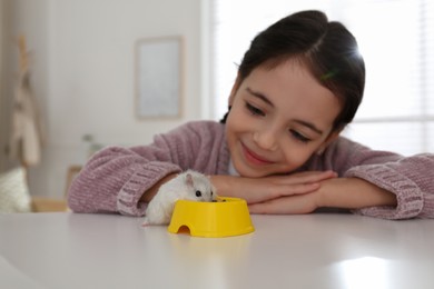 Little girl with cute hamster at table indoors
