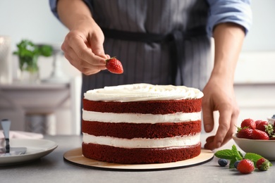 Photo of Woman decorating delicious homemade red velvet cake with strawberry at table