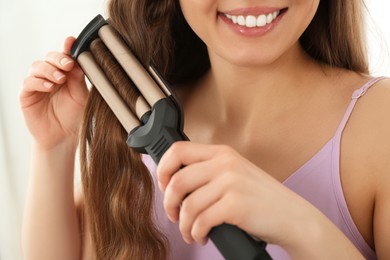 Young woman using modern curling iron on white background, closeup