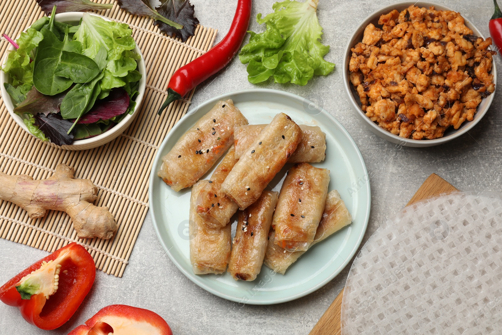 Photo of Tasty fried spring rolls and ingredients on grey table, flat lay