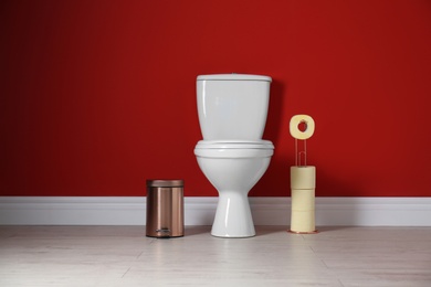 Toilet bowl with paper rolls and trash bin in restroom