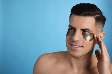 Photo of Man applying dark under eye patch on light blue background. Space for text