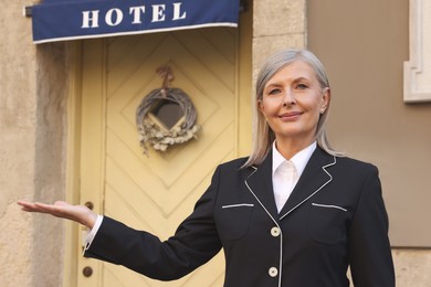 Photo of Happy business owner inviting to come into her hotel outdoors