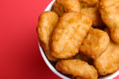 Photo of Bucket with delicious chicken nuggets on red background, top view