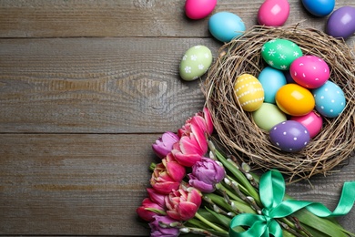 Photo of Bright painted eggs and spring tulips on wooden table, flat lay with space for text. Happy Easter