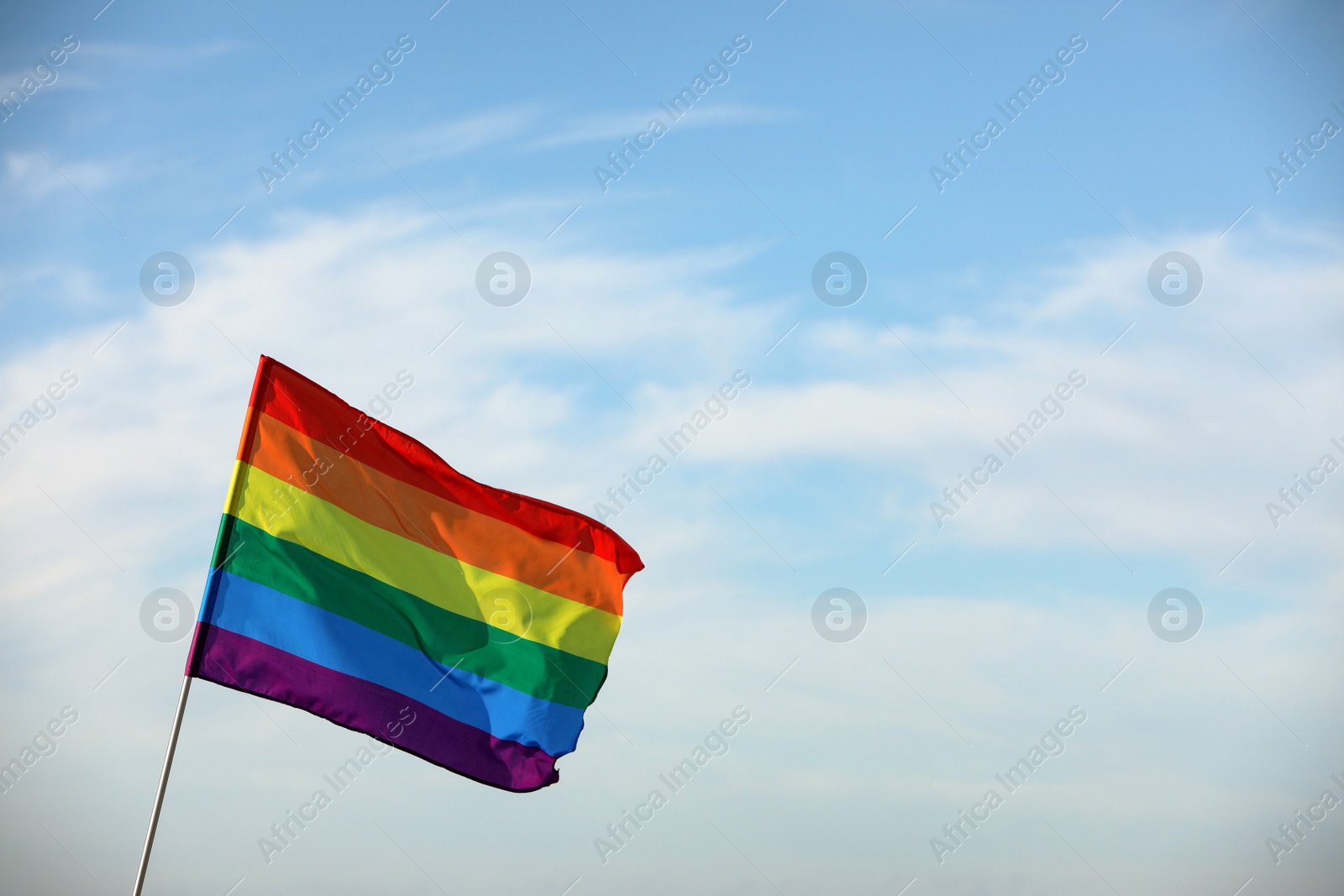 Photo of Bright LGBT flag against blue sky with clouds, space for text