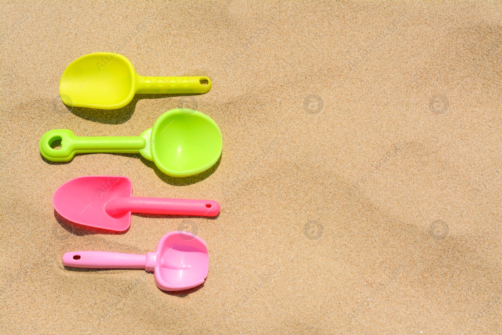 Photo of Colorful plastic shovels on sand, space for text. Beach toys