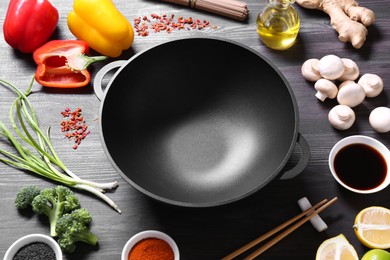 Photo of Empty iron wok and chopsticks surrounded by ingredients on dark grey wooden table