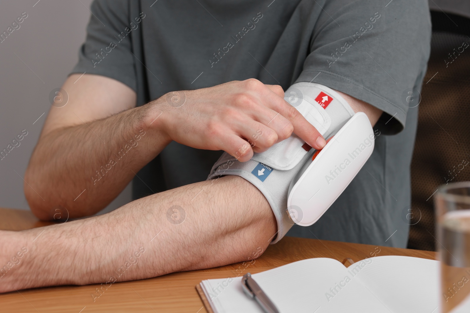 Photo of Man measuring his blood pressure with tonometer at wooden table indoors, closeup