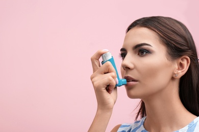 Young woman using asthma inhaler on color background. Space for text