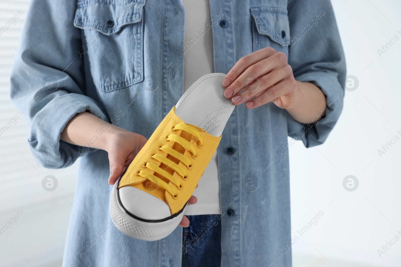 Photo of Woman putting orthopedic insole into shoe on blurred background, closeup. Foot care