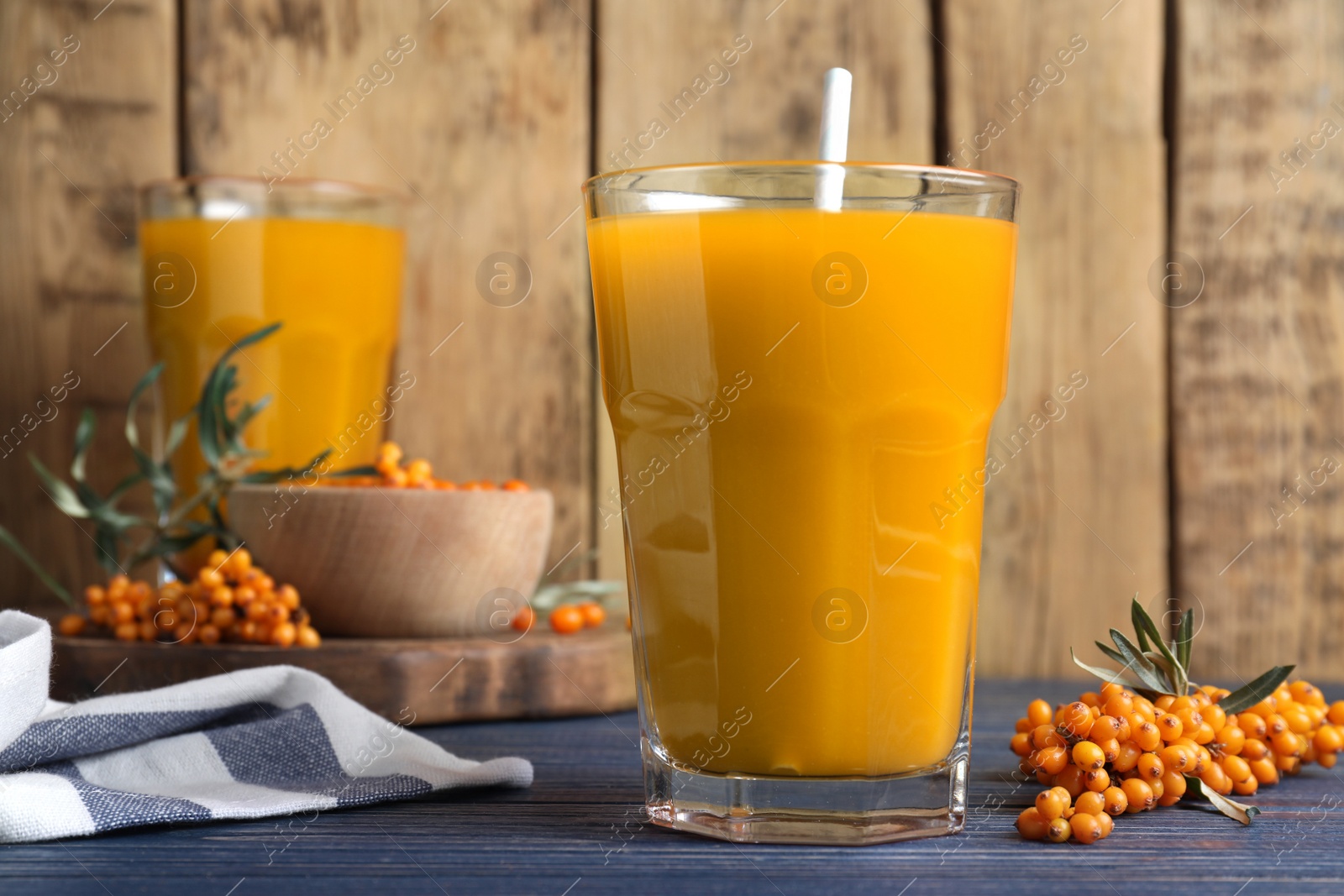 Photo of Sea buckthorn juice and fresh berries on blue wooden table, closeup