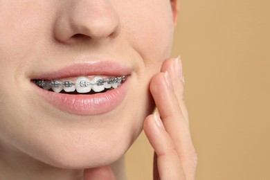 Photo of Smiling woman with dental braces on beige background, closeup. Space for text