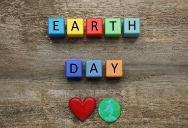Photo of Colorful cubes with words Earth Day, decorative heart and plasticine planet on wooden table, flat lay