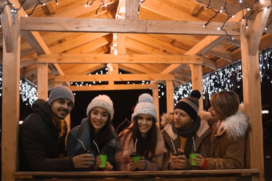 Happy friends with cups of mulled wine at winter fair