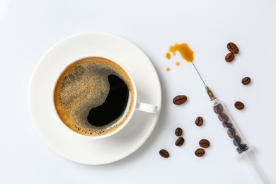 Photo of Cup of coffee and syringe with beans on white background, flat lay. Caffeine addiction concept