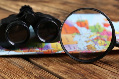 Magnifying glass, modern binoculars and map on wooden table, closeup