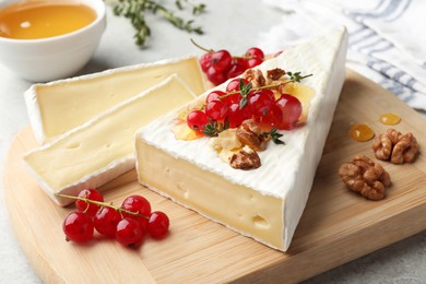 Photo of Brie cheese served with red currants, walnuts and honey on table, closeup