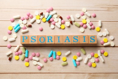 Photo of Word Psoriasis made of cubes with letters and different pills on white wooden table, flat lay